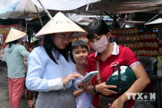 Tổ công nghệ số Đoàn Thanh niên xã Long Sơn cài đặt và hướng dẫn tiểu thương tại khu vực bán hàng hải sản phía trước Nhà lớn Long Sơn. (Ảnh: Đoàn Mạnh Dương/TTXVN)